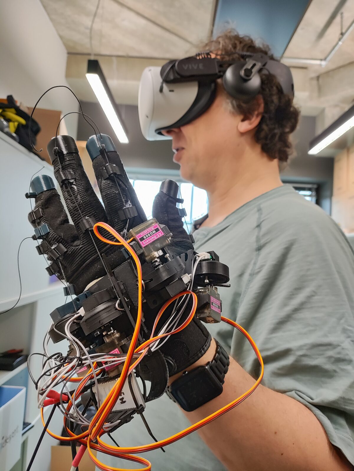 Ulrich Norbisrath wearing a VR headset and a student-built haptic glove with servo motors, testing the prototype.